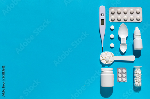 White medical treatment kit flat lay. Thermometer, bottle with pills, nasal drops, blister on blue background.