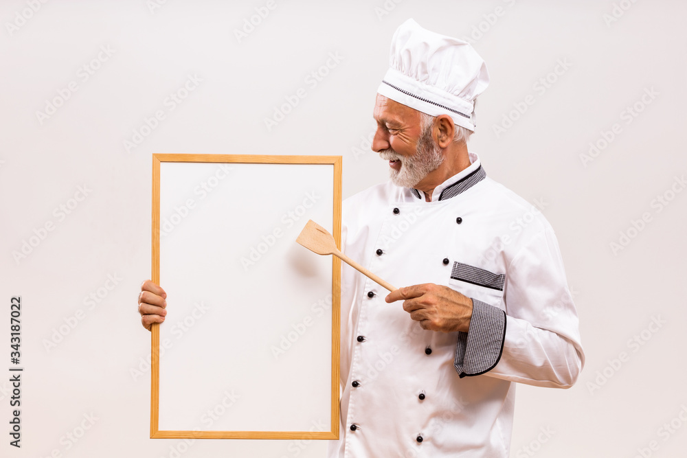 Portrait of senior chef showing with wooden spoon whiteboard on gray background. Portrait of senior chef showing with wooden spoon whiteboard on gray background.