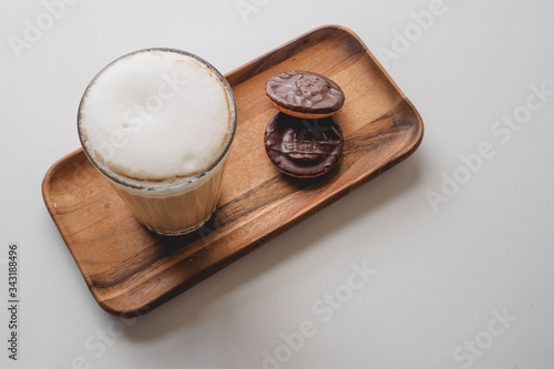 Obraz na płótnie Chocolate biscuits with a cappuccino in a glass on a wooden tray on a white table