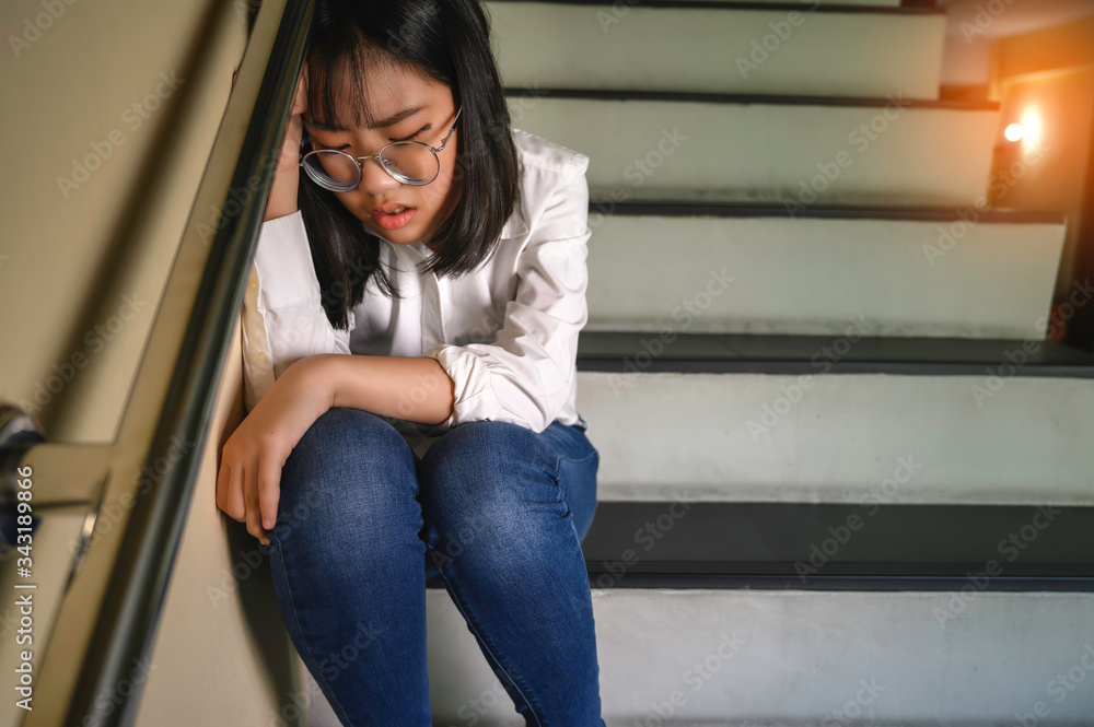 Fototapeta premium A depressed girl sitting on the stairs in the house