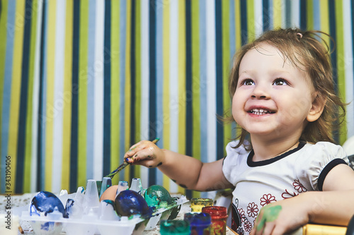 Happy little girl decorating eggs. Toddler taking brush