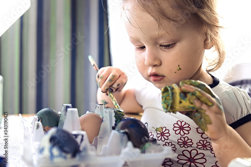 Drabble little girl painting eggs. Baby girl drowing and taking paint bush