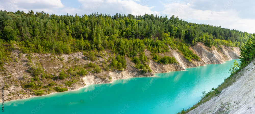 Turquoise river between small mountains with forest. Amazing summer landscape with blue sky and white clouds. Paradise place for romantic travel, to dream in silence looking into deep clear water.