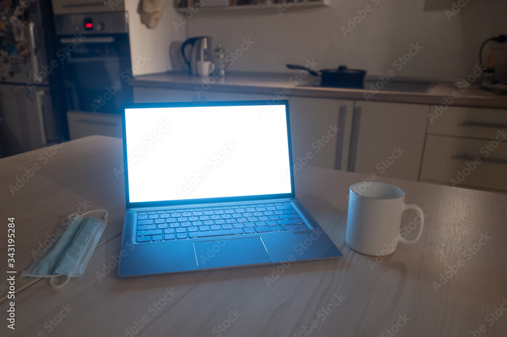 The kitchen is flat. The working atmosphere in the apartment. Laptop in the dark late at night. Work overtime in the home office. Mug and medical mask on the table. The kitchen is flat. The working atmosphere in the apartment. Laptop in the dark late at night. Work overtime in the home office. Mug and medical mask on the table.