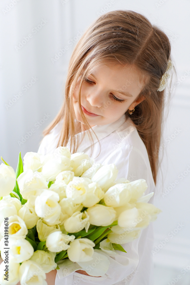 Portrait of beautiful pretty girl with white flowers tulips sitting on chair, smiling. Indoor photo. Portrait of beautiful pretty girl with white flowers tulips sitting on chair, smiling. Indoor photo.
