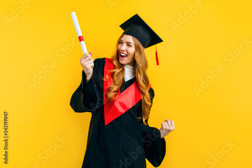 graduate girl with a diploma, shows a gesture of victory and success, on a yellow background. photo