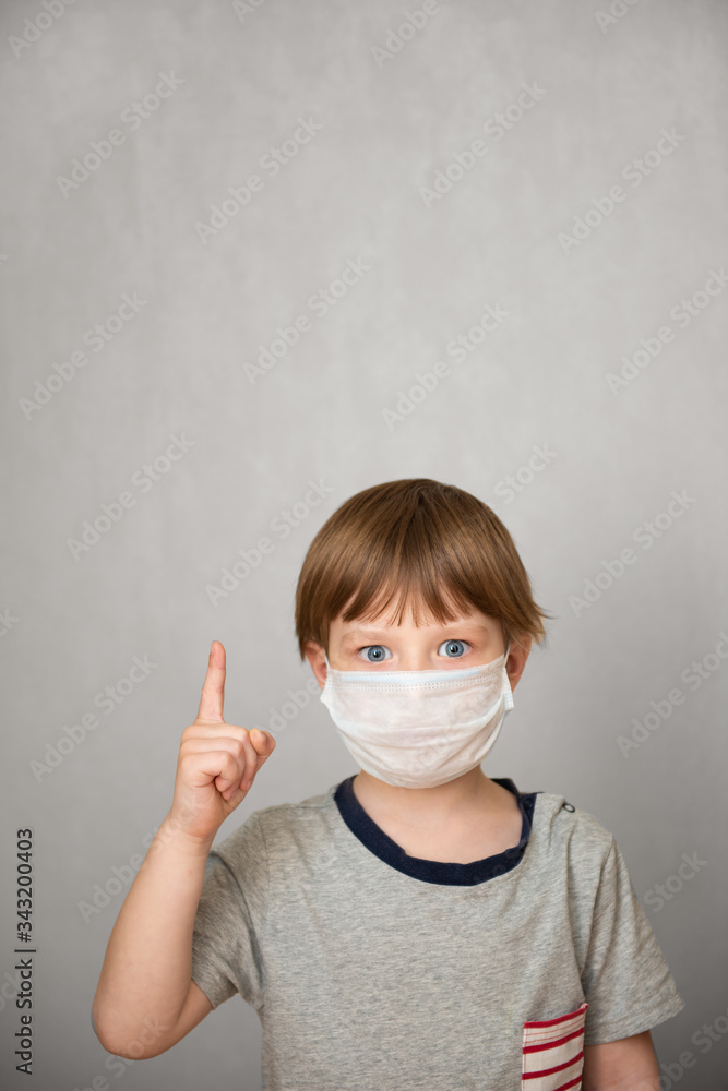Young child boy wearing health mask shows the index finger up against gray background. Healthcare information about corona virus concept. Novel Coronavirus Young child boy wearing health mask shows the index finger up against gray background. Healthcare information about corona virus concept. Novel Coronavirus