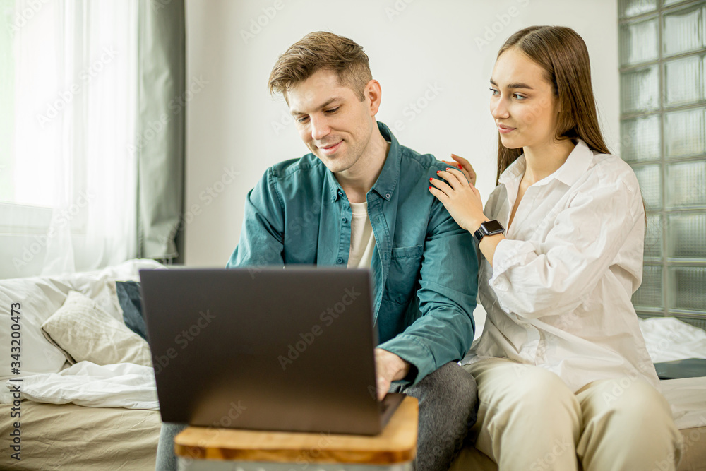 stay home. beautiful caucasian couple at home, man get support and care from a loved one during work at home, he is in freelance during quarantine coronavirus, he use laptop. wife sit next to him stay home. beautiful caucasian couple at home, man get support and care from a loved one during work at home, he is in freelance during quarantine coronavirus, he use laptop. wife sit next to him
