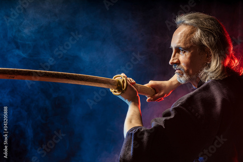 mature caucasian kendo fighter in traditional dress outfit stand with shinai in hands, going to fight with enemy, posing at camera isolated over colorful smoky space