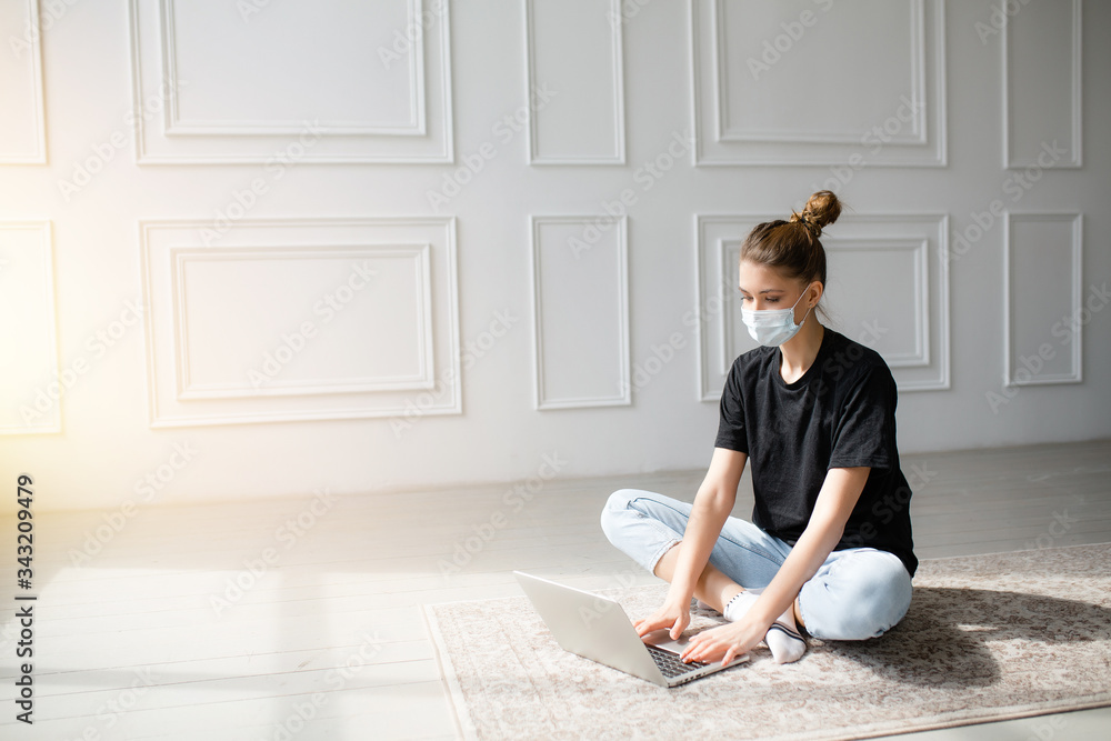 Girl in a mask sits at home and is engaged in online courses and trainings through a laptop. Self-education during quarantine. Girl in a mask sits at home and is engaged in online courses and trainings through a laptop. Self-education during quarantine.