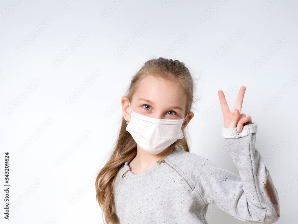 Blonde little girl in gray jumper and medical mask, posing isolated on white. She is looking at you and showing victory hand. Coronavirus. Quarantine. Worldwide pandemic COVID-19. Close up, copy space Blonde little girl in gray jumper and medical mask, posing isolated on white. She is looking at you and showing victory hand. Coronavirus. Quarantine. Worldwide pandemic COVID-19. Close up, copy space