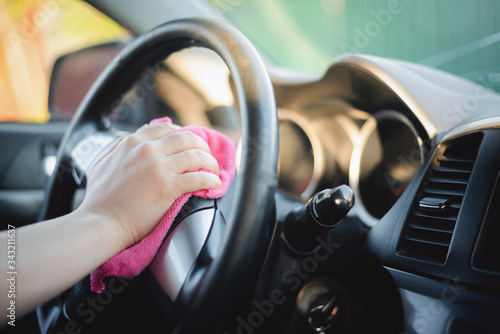 The cleaner wipes and polishes the car steering wheel with a rag close up.