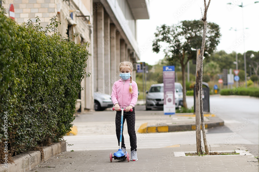 little girl in medical mask on children's scooter during quarantine