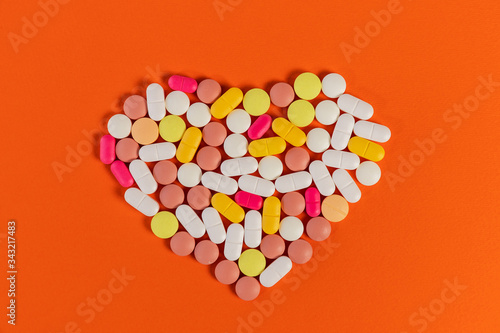 Many different pills and tablets folded in shape of heart on orange background. Many pills and tablets with space for text. Health care. Top view. Copy space. New image. Pharmaceutical pills. Closeup