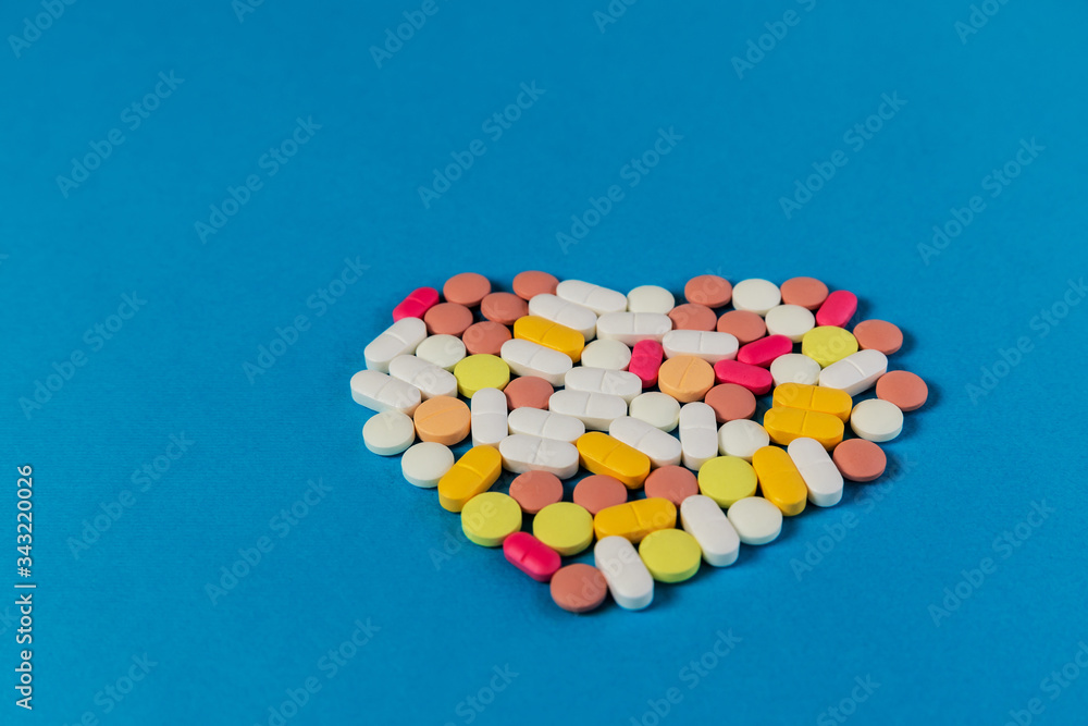 Many different pills and tablets folded in shape of heart on blue background. Many pills and tablets. Space for text. Health care. Top view. Copy space. New image. Pharmaceutical. Closeup. Soft focus Many different pills and tablets folded in shape of heart on blue background. Many pills and tablets. Space for text. Health care. Top view. Copy space. New image. Pharmaceutical. Closeup. Soft focus