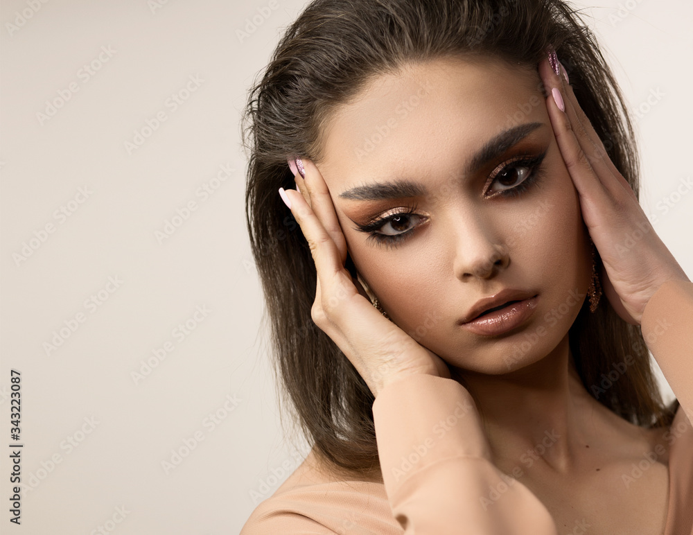 Fototapeta premium Close-up face of a young woman. She holds her palms near her temples and looks straight. Fashionable pose, stretch the skin near the eyes.