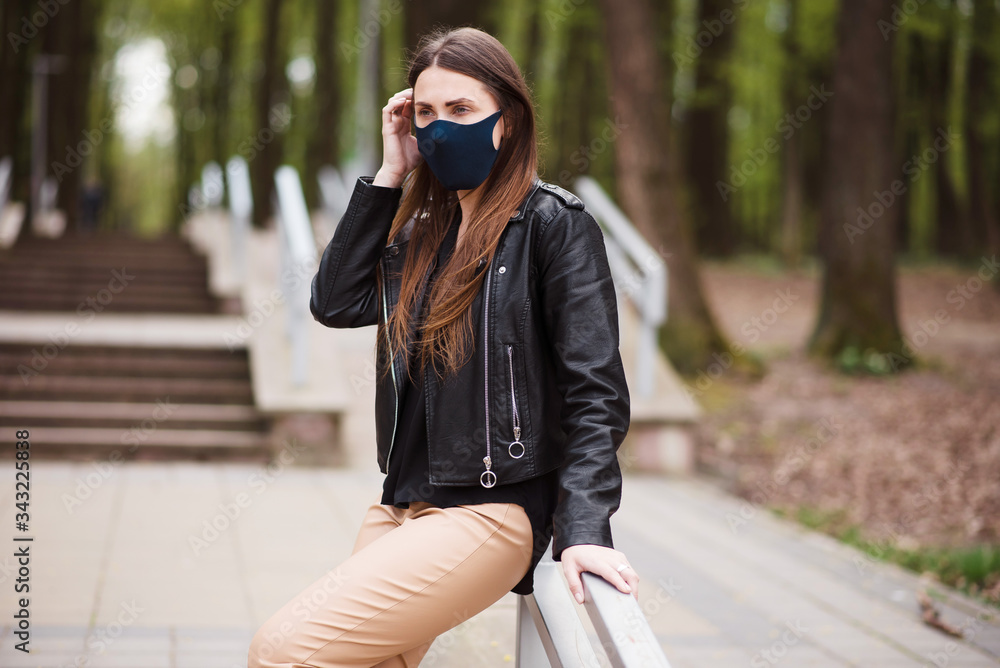 Young brunette wearing protective mask walking after quarantine. A woman stands leaning on the handrail in the park on a spring day. Walks in the open air Young brunette wearing protective mask walking after quarantine. A woman stands leaning on the handrail in the park on a spring day. Walks in the open air