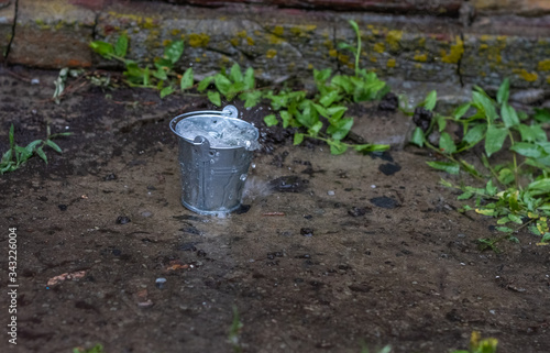 a bucket of water in which water splashes. A green plant grows from asphalt.