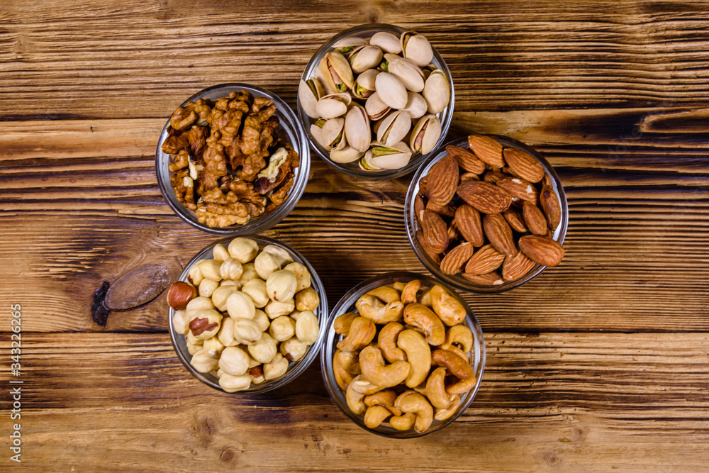 Various nuts (almond, cashew, hazelnut, pistachio, walnut) in glass bowls on a wooden table. Vegetarian meal. Healthy eating concept. Top view Various nuts (almond, cashew, hazelnut, pistachio, walnut) in glass bowls on a wooden table. Vegetarian meal. Healthy eating concept. Top view
