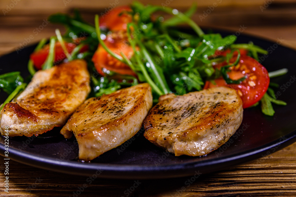 Roasted chicken breasts and salad with arugula and cherry tomatoes in a black plate Roasted chicken breasts and salad with arugula and cherry tomatoes in a black plate