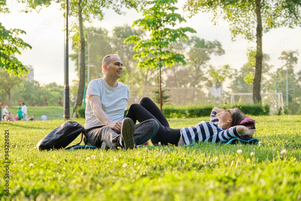 Middle-aged couple sitting on yoga mat, man and woman talking relaxing drinking water Middle-aged couple sitting on yoga mat, man and woman talking relaxing drinking water