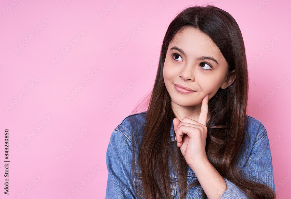 Cute emotional caucasian girl in a denim jacket on a pink background.