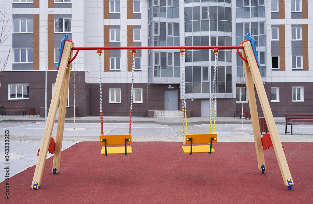Swing for children on a new playground against the background of a new apartment building