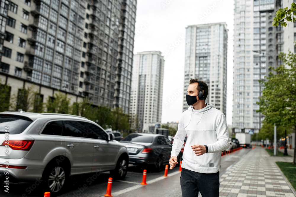 Keep yourself in shape during quarantine. Athletic young man is jogging in a protective mask among high-rise buildings. Healthy lifestyle concept Keep yourself in shape during quarantine. Athletic young man is jogging in a protective mask among high-rise buildings. Healthy lifestyle concept