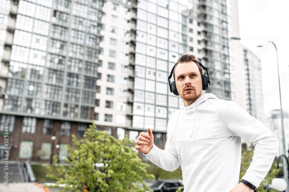 Workout outdoors. Young athletic guy in sportswear with headphones runs in an urban landscape Workout outdoors. Young athletic guy in sportswear with headphones runs in an urban landscape