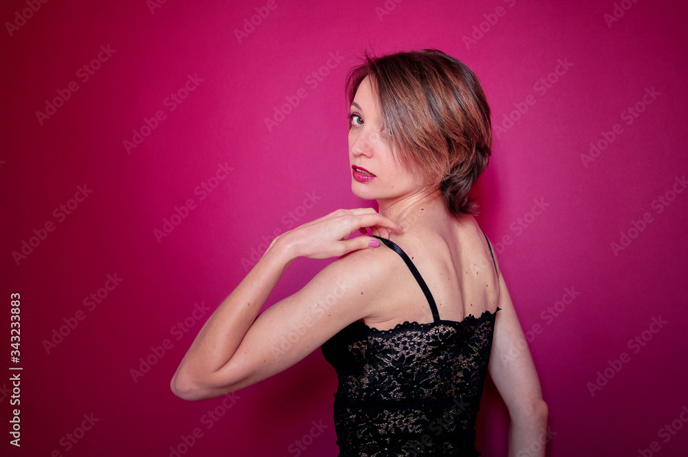 Young woman with short hair dressed in black lace bustier and blue jeans is posing in the studio on bright pink background Young woman with short hair dressed in black lace bustier and blue jeans is posing in the studio on bright pink background