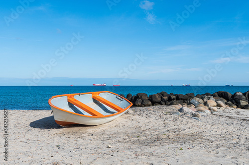 Small boat on beach with boulders and cargo ships in the background near Skagen, Denmark