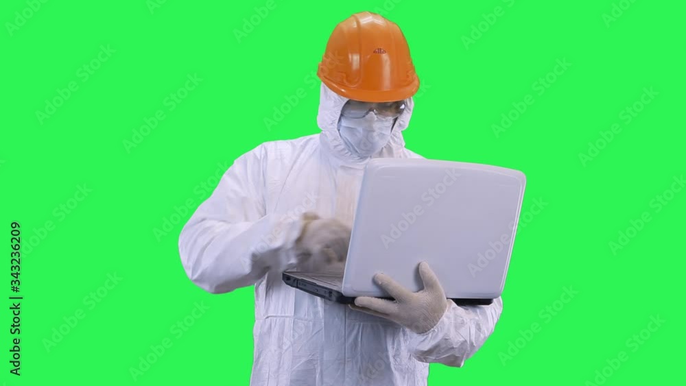 A man in a helmet and protective suit enters data into a computer and looks at what is happening.Green screen background. A man in a helmet and protective suit enters data into a computer and looks at what is happening.Green screen background.