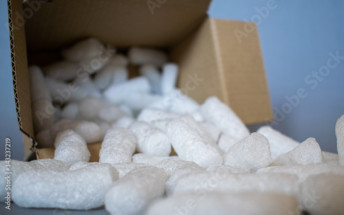 Open cardboard box with white styrofoam filling pieces comming out, parcel packing materials, safe and secure shipment methods, grey background