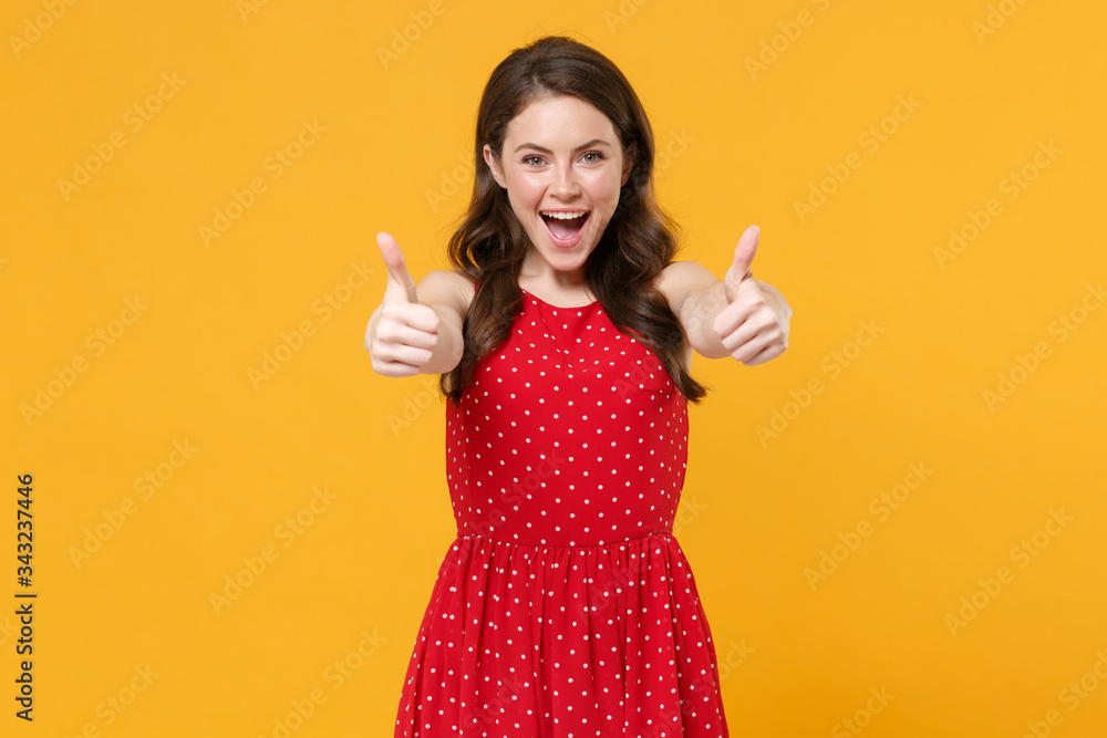 Excited funny young brunette woman girl in red summer dress posing isolated on yellow wall background studio portrait. People sincere emotions lifestyle concept. Mock up copy space. Showing thumbs up. Excited funny young brunette woman girl in red summer dress posing isolated on yellow wall background studio portrait. People sincere emotions lifestyle concept. Mock up copy space. Showing thumbs up.