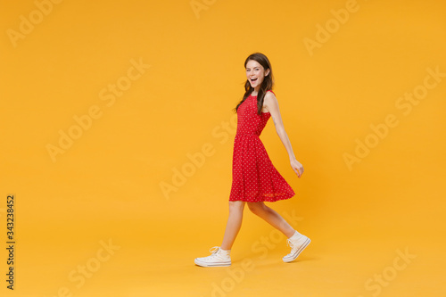 Side view of cheerful young brunette woman girl in red summer dress posing isolated on yellow background studio portrait. People sincere emotions lifestyle concept. Mock up copy space. Looking camera.