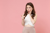Shocked young brunette woman girl in light casual clothes posing isolated on pastel pink background studio. People lifestyle concept. Mock up copy space. Pointing index finger aside put hand on cheek.