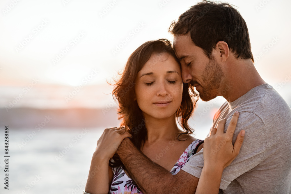 Loving young couple standing together on a beach at dusk Loving young couple standing together on a beach at dusk