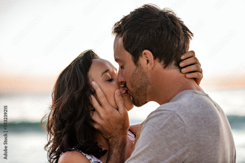 Loving couple sharing a kiss on a beach at dusk Loving couple sharing a kiss on a beach at dusk