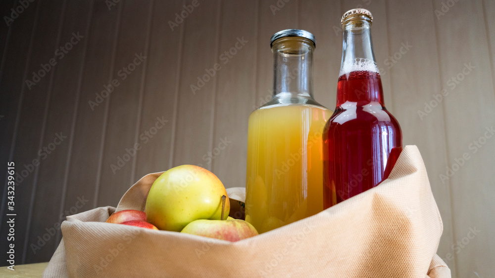 Bottles of apple juice and cider lies in an eco bag with apples on a wooden table. Bottles of apple juice and cider lies in an eco bag with apples on a wooden table.