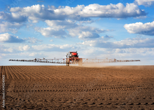 Big red sprayer with long arms at the arable field makes fertilizers in early...