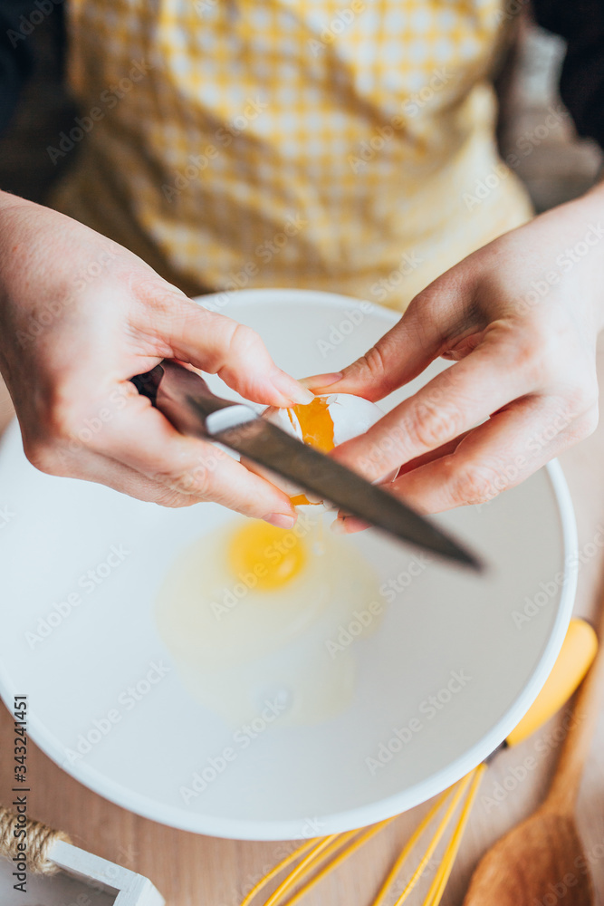 A woman is preparing a custard dough for baking - breaks an egg in a bowl - home cooking A woman is preparing a custard dough for baking - breaks an egg in a bowl - home cooking