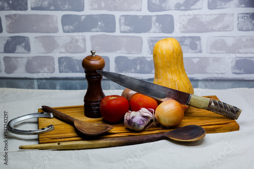 still life of fresh vegetables tomatoes garlic pumpkin onion cutting board spoons and blade