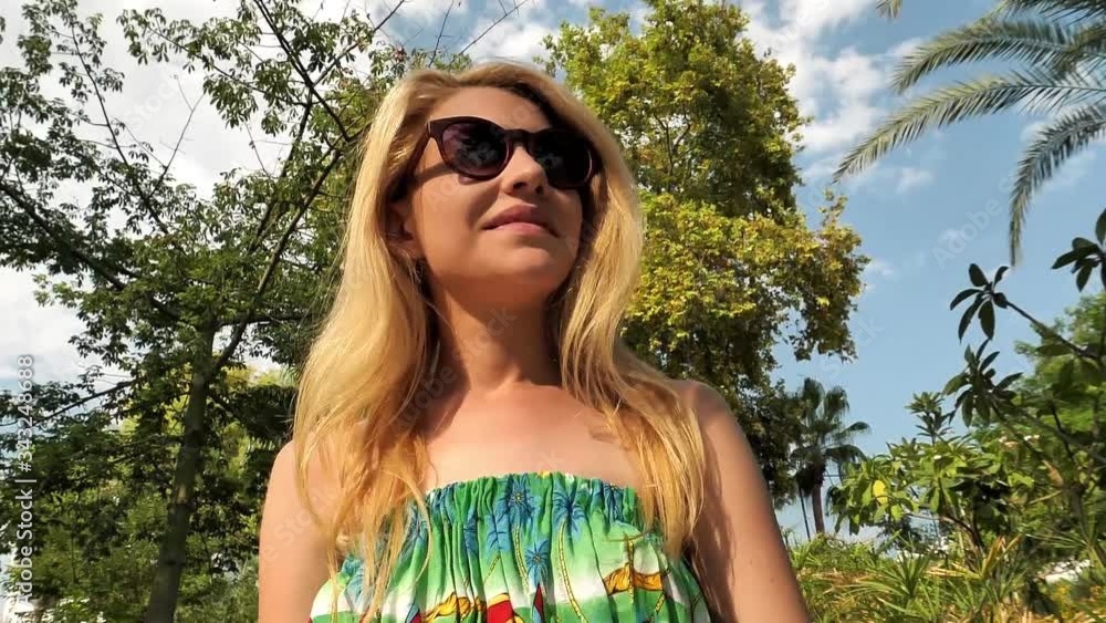 Blonde girl walks in a tropical park straightening her hair. Blonde girl walks in a tropical park straightening her hair.