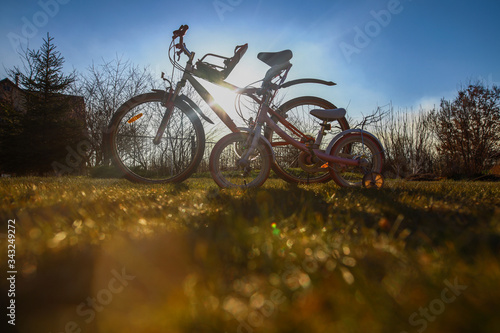 Two bicycles - adult and kid's one - standing outside in beautiful sunlight on green grass lane, bottom view, togetherness concept, kids bike seat