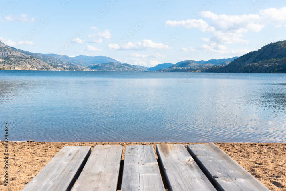 Picnic table on sandy beach with view of lake, mountains, and blue sky