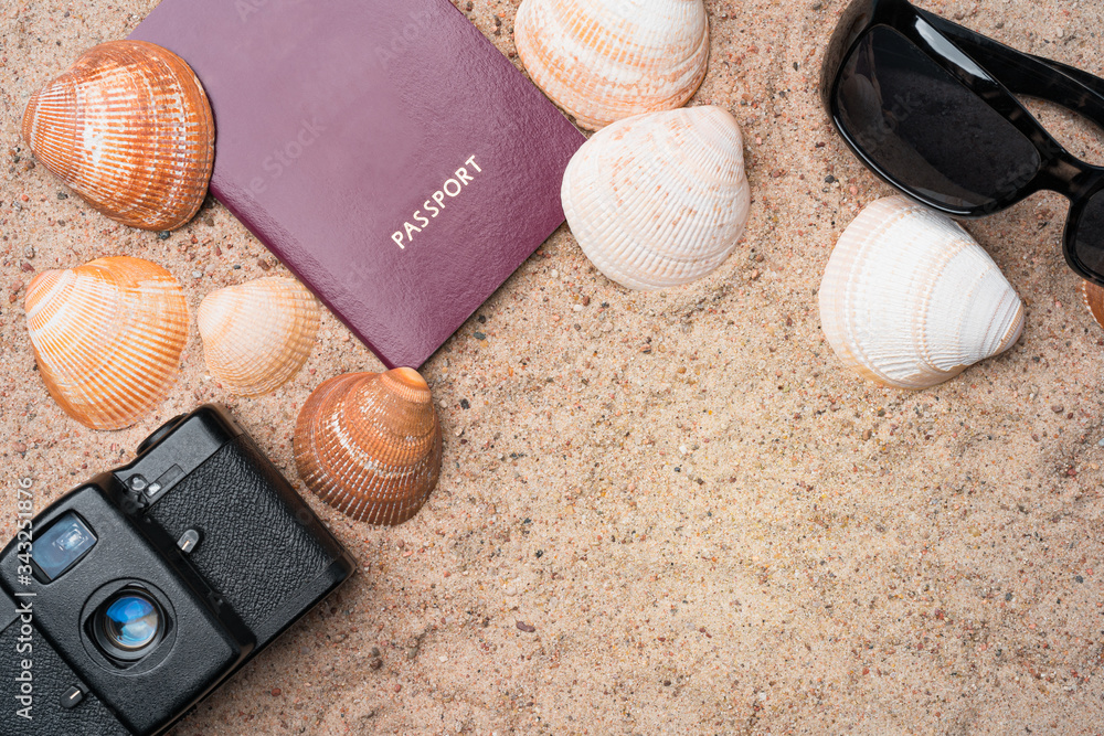 Passport, vintage film camera, sunglasses and seashells on golden beach sand. Summer travel abstract concept. Copy space in the bottom right corner.