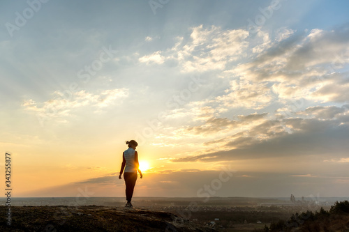 Silhouette of a woman hiker standing alone enjoying sunset outdoors. Female tourist on rural field in evening nature. Tourism  traveling and healthy lifestyle concept.