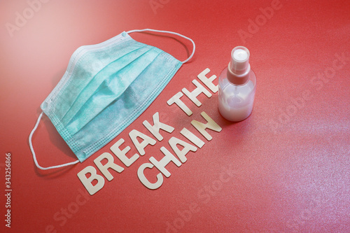 A face mask with a bottle of hand sanitizer with wood lettering on a red background.  Message on virus spread