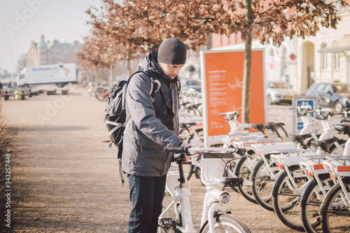 Man taking bike in bike sharing. Man take city bicycle vacation at the parking. Public electric bikes for rent parked in Copenhagen, Denmark. Save CO2 and Green energy. Person and cycle in europe