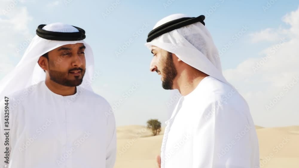 Two men with emirates white kandura traditional outfit making safari in the desert of Dubai Two men with emirates white kandura traditional outfit making safari in the desert of Dubai